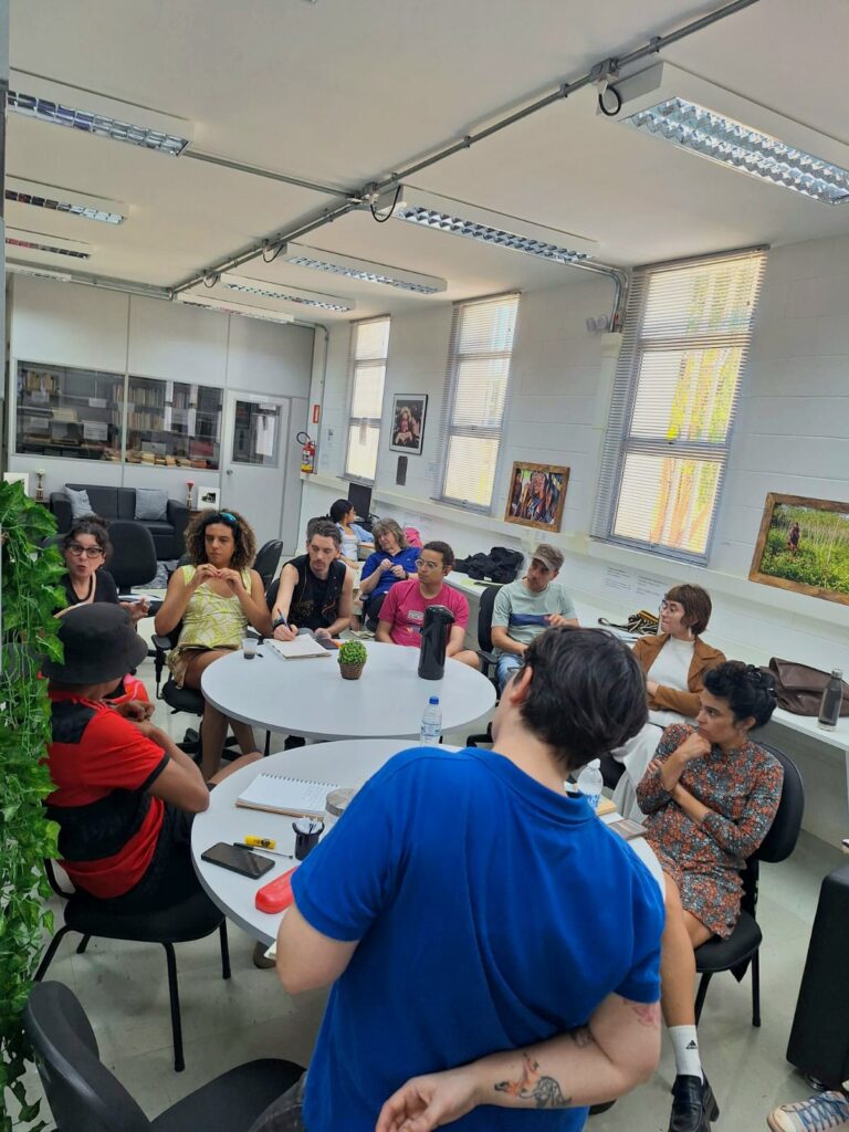 seminário de pesquisa em que Agustin (a) aparece de costas para a tela e os estudantes estão de frente. Eles estão na sala da biblioteca do PAGU
