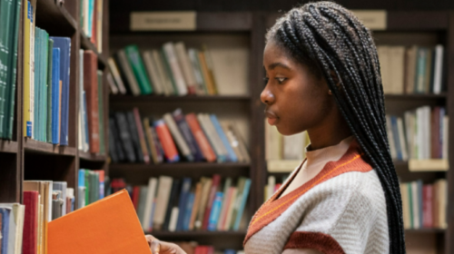 Jovem negra colocando um livro em uma estante em uma biblioteca. Reprodução/Freepik.